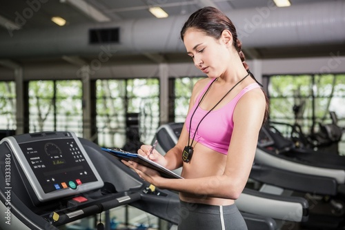 Trainer writing on a clipboard on treadmill © WavebreakMediaMicro