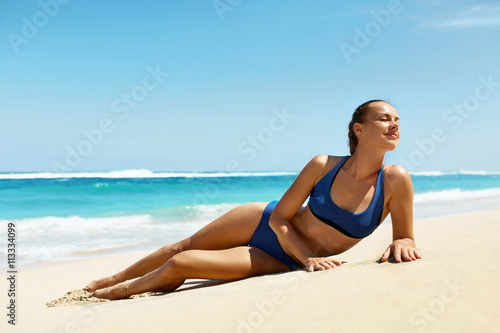 Woman On Beach In Summer. Sexy Happy Female Model Sun Tanning On Sand. Beautiful Girl With Fit Body, Healthy Tan Skin In Sport Bikini Relaxing At Luxury Sea Resort On Vacations. Summertime Relaxation