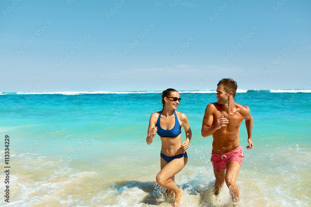 Couple Fun On Beach. Romantic People In Love Running On Sand At Luxury Sea Resort. Handsome Happy Man, Beautiful Smiling Woman Laughing Together On Summer Travel Vacation. Relationships, Summertime