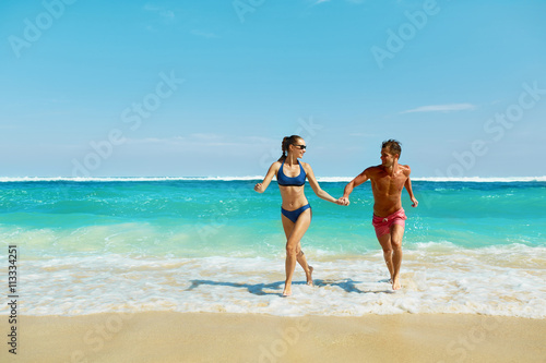 Couple Fun On Beach. Romantic People In Love Running On Sand At Luxury Sea Resort. Handsome Happy Man, Beautiful Smiling Woman Laughing Together On Summer Travel Vacation. Relationships, Summertime