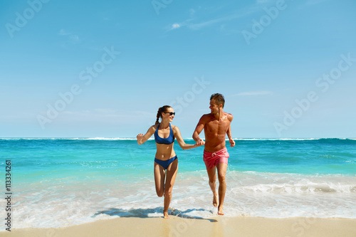 Couple Fun On Beach. Romantic People In Love Running On Sand At Luxury Sea Resort. Handsome Happy Man, Beautiful Smiling Woman Laughing Together On Summer Travel Vacation. Relationships, Summertime
