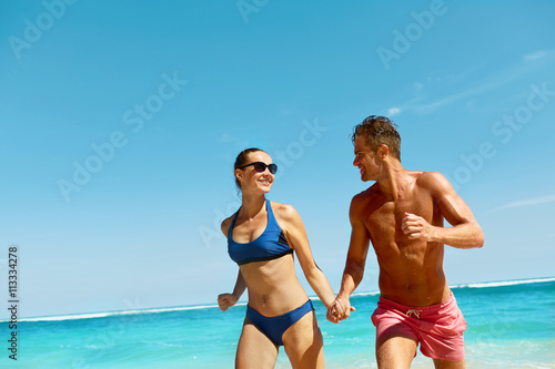 Couple Fun On Beach. Romantic People In Love Running On Sand At Luxury Sea Resort. Handsome Happy Man, Beautiful Smiling Woman Laughing Together On Summer Travel Vacation. Relationships, Summertime © puhhha