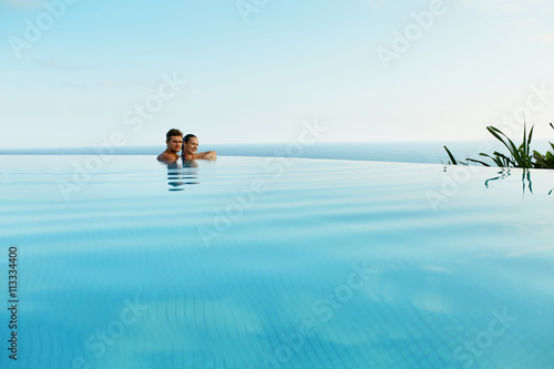 Couple In Love At Luxury Resort On Romantic Summer Vacation. People Relaxing Together In Edge Swimming Pool Water, Enjoying Beautiful Sea View. Happy Lovers On Honeymoon Travel. Relationship, Romance © puhhha
