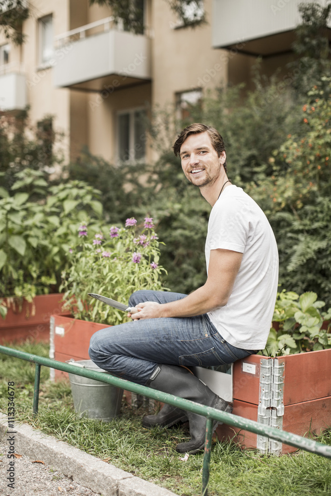 Full length portrait of young man with gardening equipment sitting in garden Full length portrait of young man with gardening equipment sitting in garden