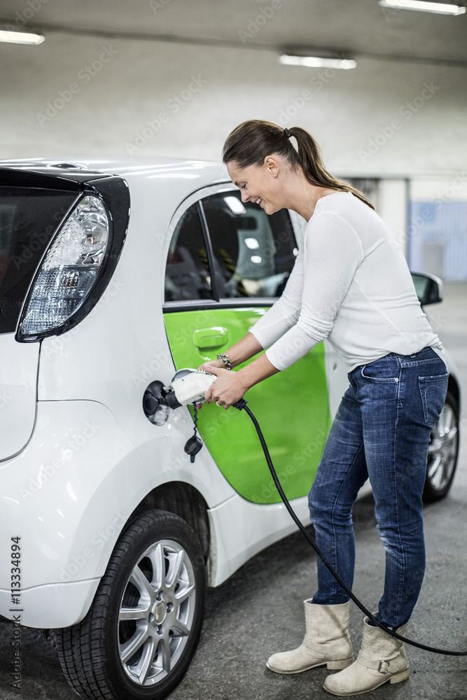 Full length of woman charging electric car at gas station Full length of woman charging electric car at gas station