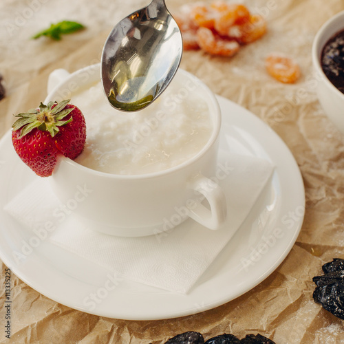 Rice porrige with strawberry and oil spoon on parchment background