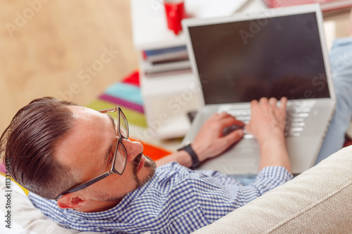 Closeup portrait of handsome businessman lying on sofa or couch with laptop computer. Man in glasses looking away.