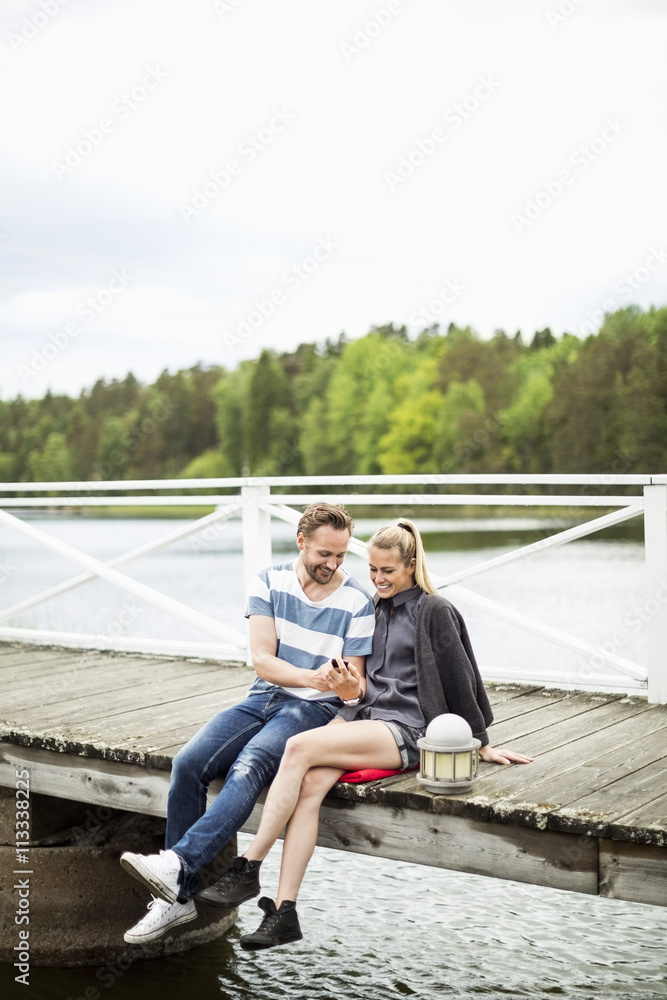 Couple using mobile phone together on pier Couple using mobile phone together on pier
