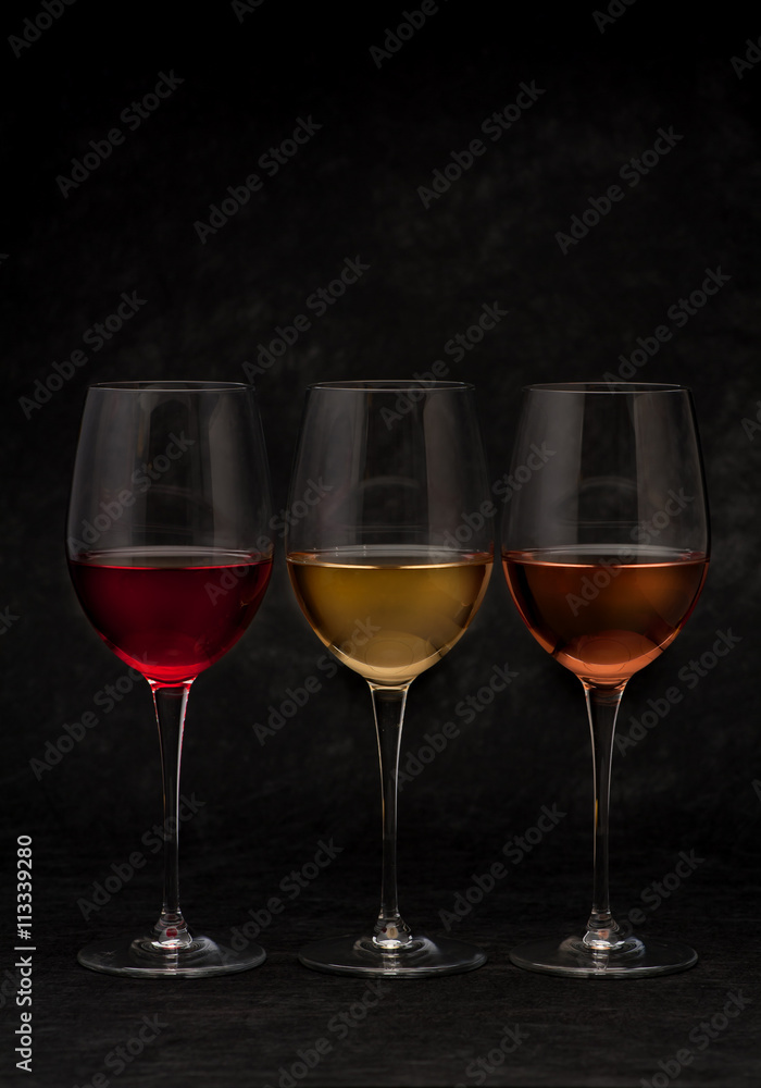 Red, pink and white wine in glasses on black grunge background