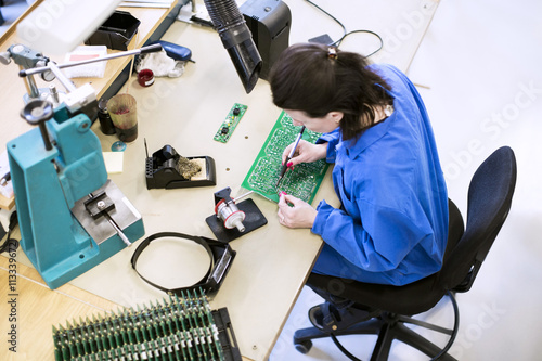 High angle view of female technician soldering circuit board at desk in factory photo