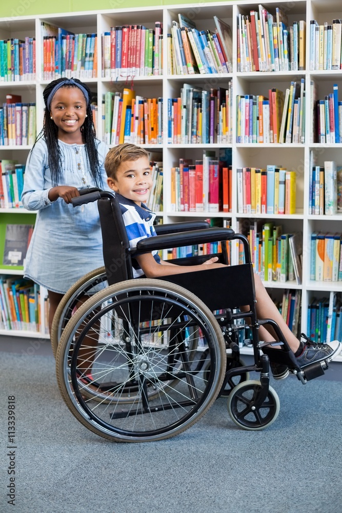 Obraz premium Happy schoolgirl standing with schoolboy on wheelchair