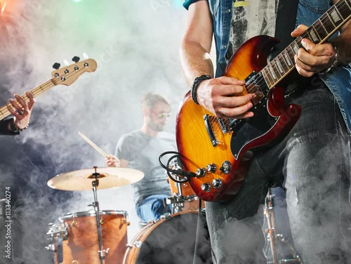 Obraz Zespół rockowy występuje na scenie. Gitarzysta, gitara basowa i perkusja. Gitarzysta na pierwszym planie. Zbliżenie.