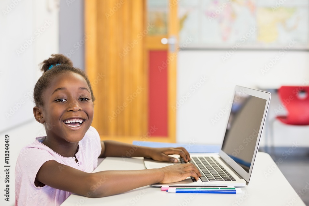Smiling schoolgirl using laptop in classroom Smiling schoolgirl using laptop in classroom