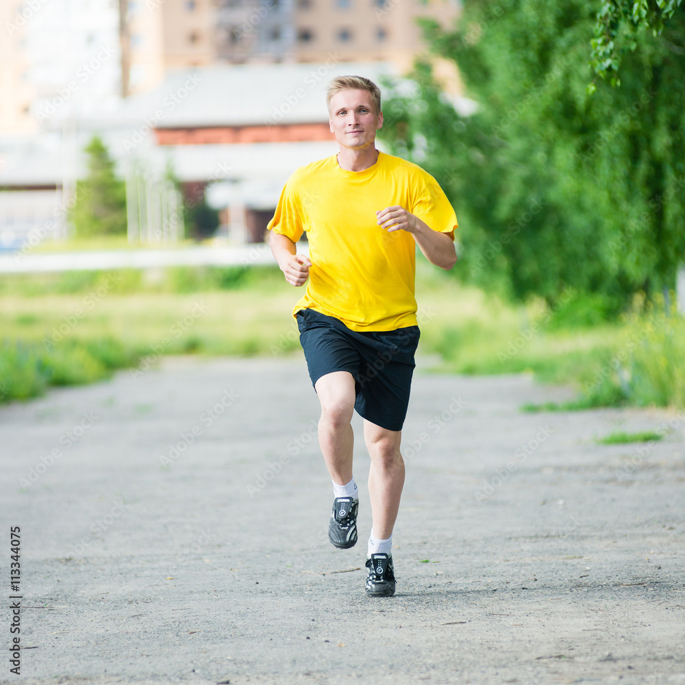 Running man jogging in city street park at beautiful summer day. Sport fitness model caucasian ethnicity training outdoor.