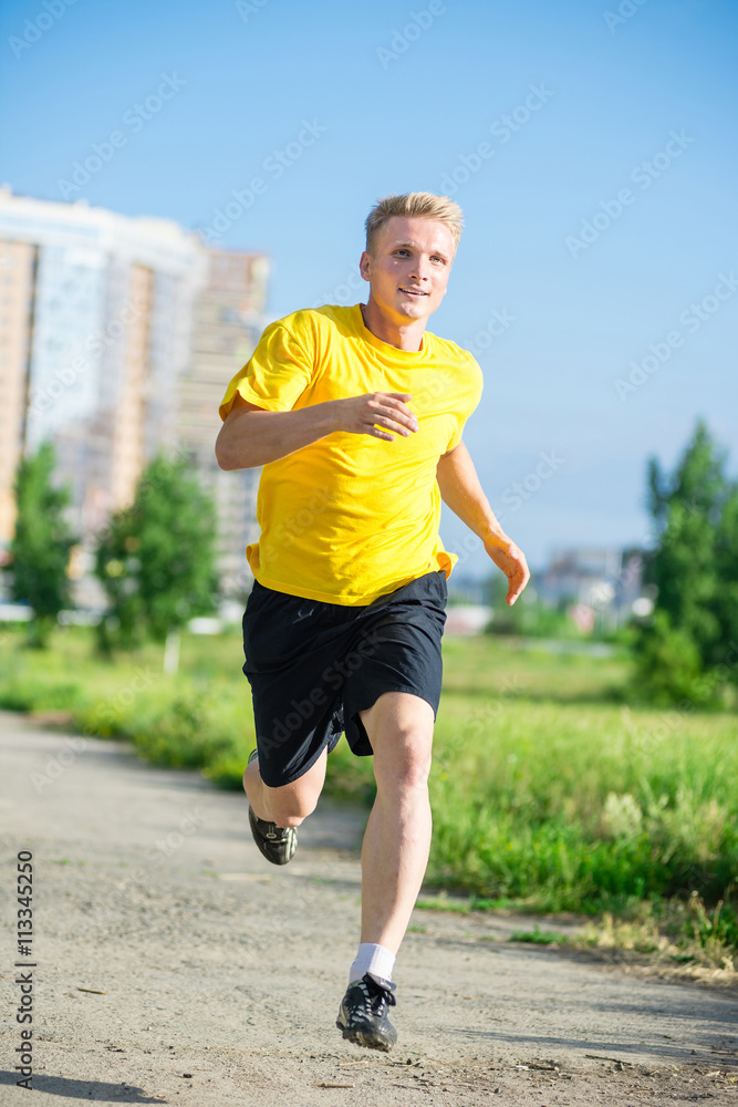 Running man jogging in city street park at beautiful summer day. Sport fitness model caucasian ethnicity training outdoor. Running man jogging in city street park at beautiful summer day. Sport fitness model caucasian ethnicity training outdoor.