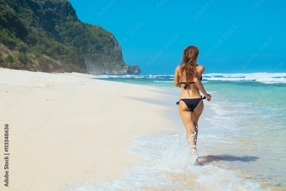 Woman running through sea water on a beach in Bali. Female runner jogging during outdoor workout on beach.