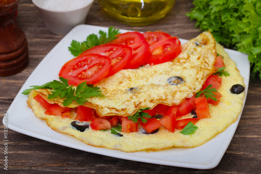 Breakfast, tasty omelet omelette scrambled eggs with tomato, olives and parsley. On a wooden background