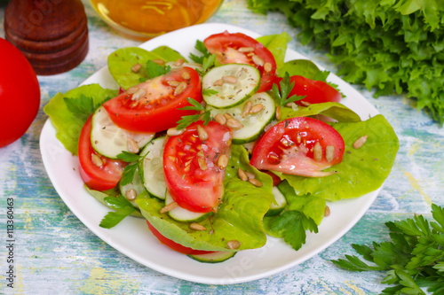 Fresh salad with tomatoes, cucumbers and lettuce on a wooden background