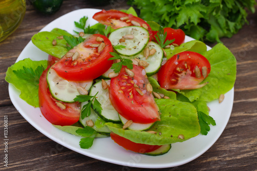 Fresh salad with tomatoes, cucumbers and lettuce on a wooden background