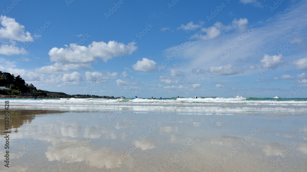 Reflets dans l'eau et surfeurs à marée basse sur la plage de Trestel en Bretagne
