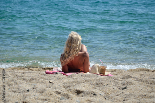 Blond woman relaxing on beach  enjoying cold coffee frappe and looking at sea