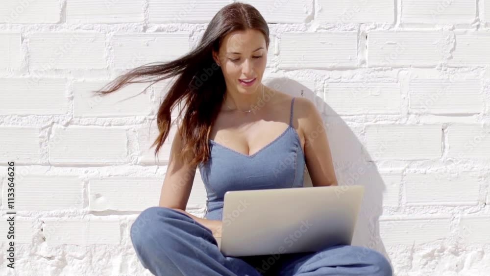 Young woman working on a laptop in the sunshine as she sits cross ...