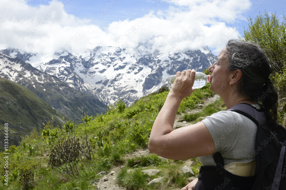 Naklejka premium Femme sur un chemin de montagne dans le parc national des Écrins buvant un peu d'eau