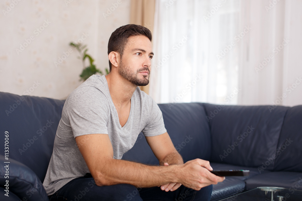Young man switching TV channel on remote control Young man switching TV channel on remote control
