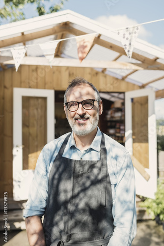 Portrait of happy mature store owner standing against shop photo