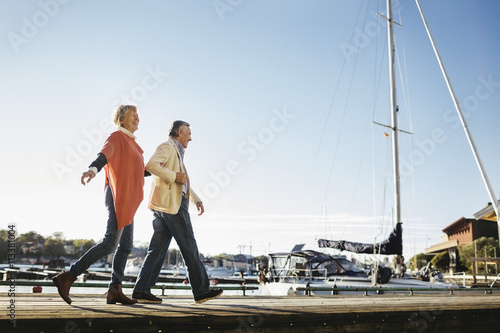 Full length of happy senior couple walking on pier against sky