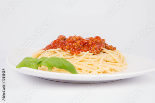 Spaghetti bolognese decorated with basil on a white background