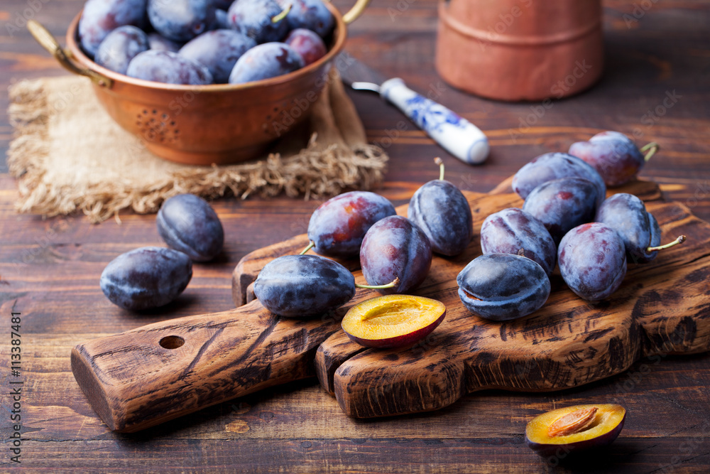 Obraz premium Fresh organic plums in copper bowl and on rustic wooden cutting board