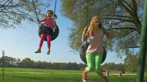 Cute little girl and her bigger sister enyoj and smile while swinging on playground.
 photo