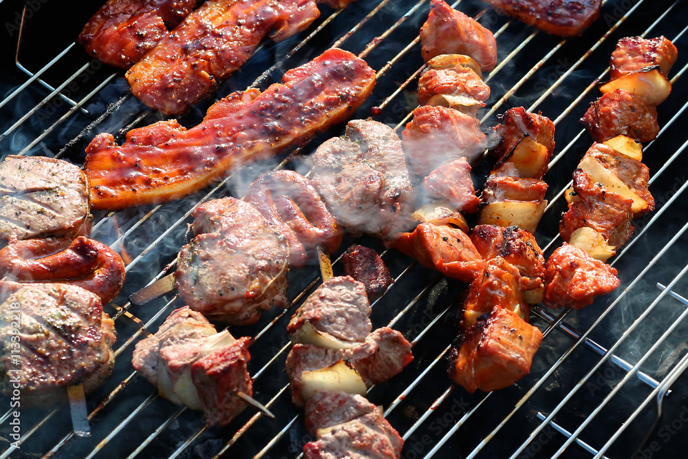 Assorted mixed grill on wooden skewers from chicken meat, lamb and pork, marinated spareribs, sausages and various vegetables roasting on barbecue grid cooked for summer family dinner Assorted mixed grill on wooden skewers from chicken meat, lamb and pork, marinated spareribs, sausages and various vegetables roasting on barbecue grid cooked for summer family dinner