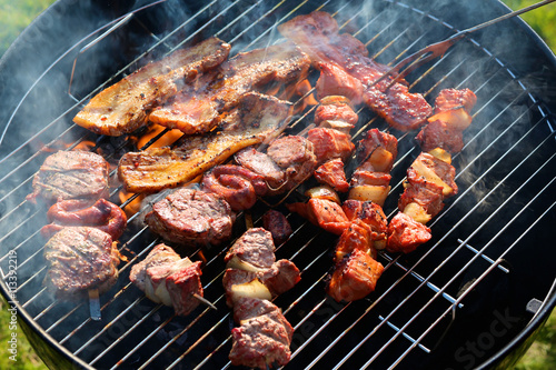 Assorted mixed grill on wooden skewers from chicken meat  lamb and pork  marinated spareribs  sausages and various vegetables roasting on barbecue grid cooked for summer family dinner