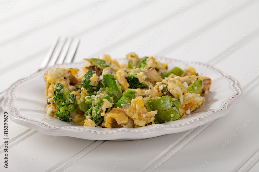 Scrambled eggs with broccoli, onions, and green bell peppers side view on white wood Scrambled eggs with broccoli, onions, and green bell peppers side view on white wood