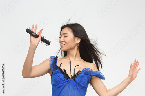 Attractive brunette holding microphone in front of her over white background. Fashion asian model in blue lingerie singing songs in studio.