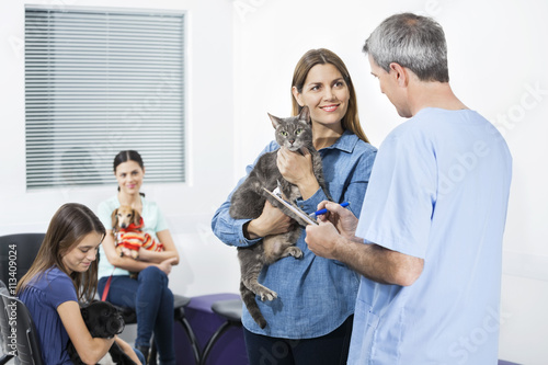 Fototapeta Naklejka Na Ścianę i Meble -  Woman Holding Cat While Looking At Nurse In Clinic