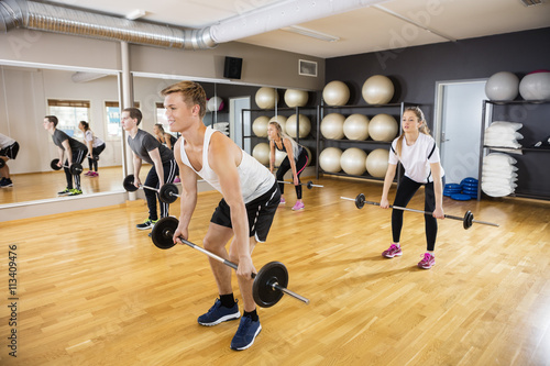 Fototapeta Naklejka Na Ścianę i Meble -  Sporty Men And Women Lifting Barbells In Gym