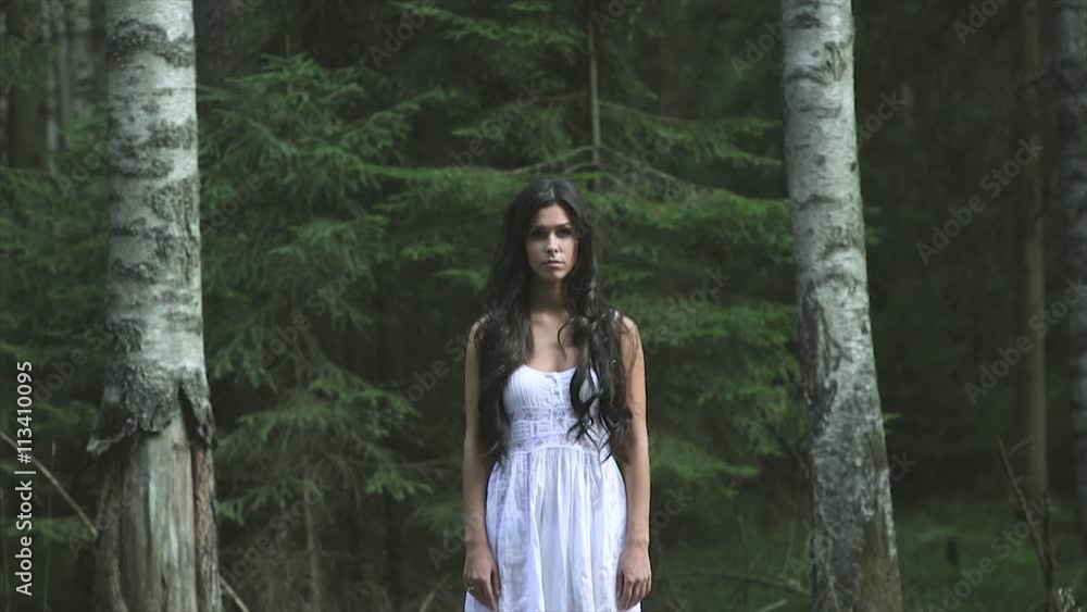 Beautiful young woman wearing elegant white dress stand between two birches in the forest Beautiful young woman wearing elegant white dress stand between two birches in the forest