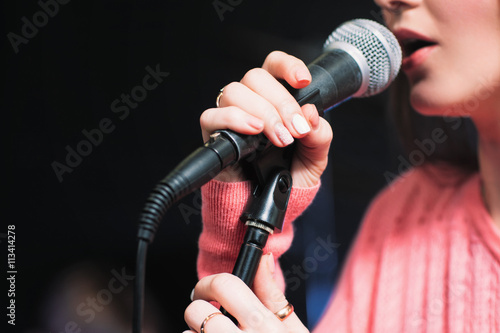Microphone and unrecognizable female singer close up. Cropped image of female singer in pink dress , singing into a microphone, holding mic with two hands. Copyspace