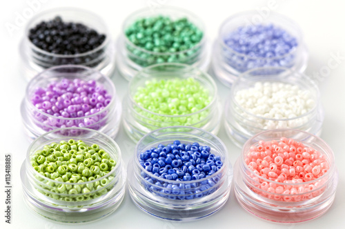 Small colorful beads on transparent round boxes on white background