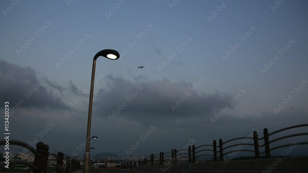Street lamp against airplane flying in cloudy dusky sky Street lamp against airplane flying in cloudy dusky sky