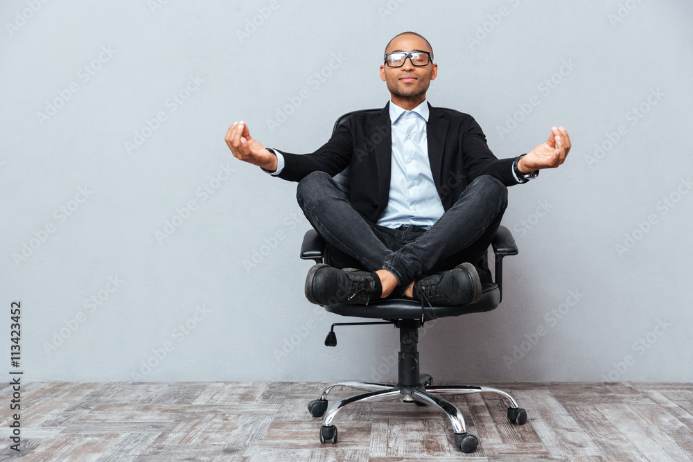 Relaxed african young man sitting and meditating on office chair - obrazy, fototapety, plakaty 