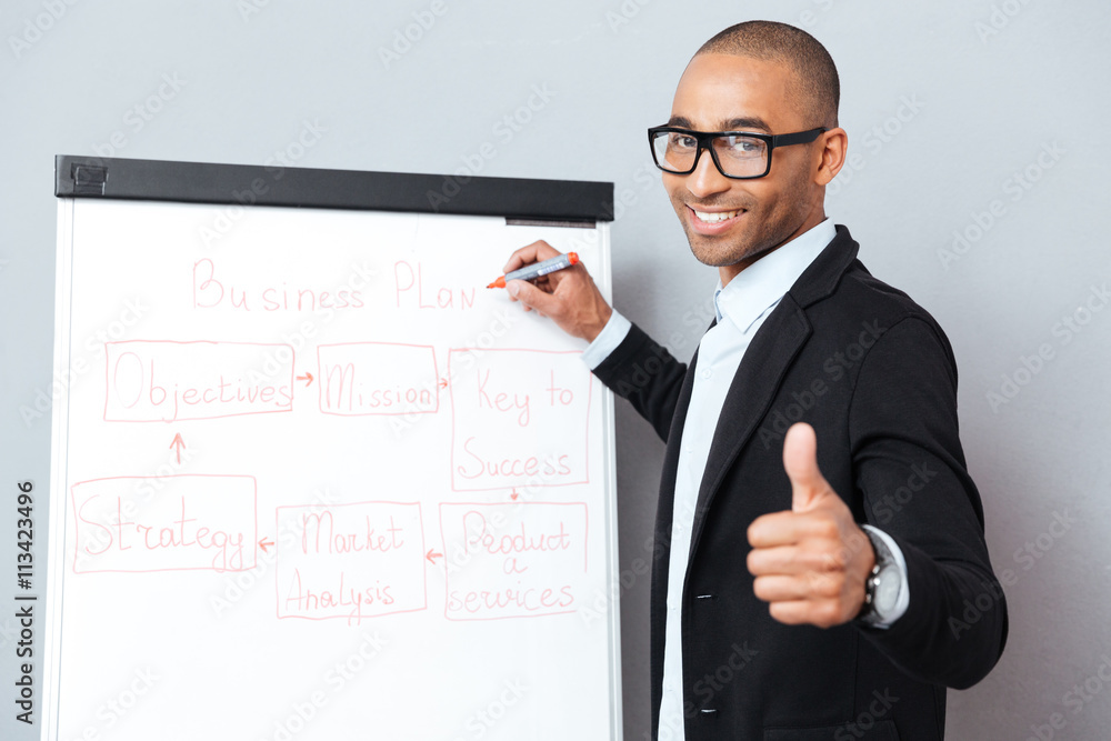 Happy african man writing on flipchart and showing thumbs up Happy african man writing on flipchart and showing thumbs up