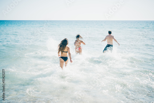 group of young multiethnic friends women and men at the beach in summertime having fun in the water splashing - happiness, friendship, having fun concept