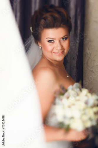 Joyful bride stand behind a window