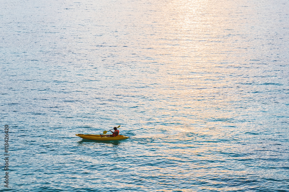 Fototapeta premium Kayak, a guy kayaking on blue ocean in sunset with sunlight reflection on the sea