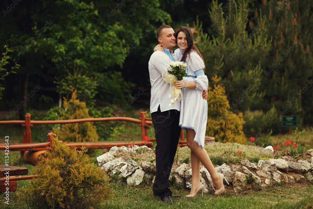 Fototapeta premium Groom in an embroidered blue shirt hugs a tender brunette bride
