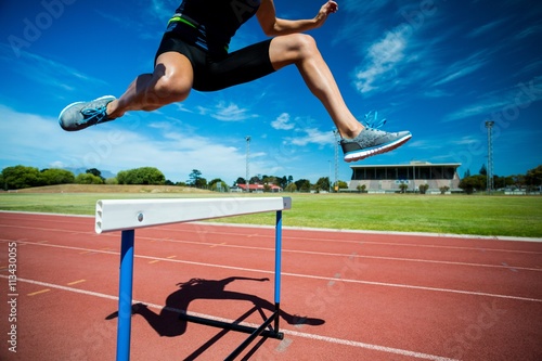 Female athlete jumping above the hurdle photo